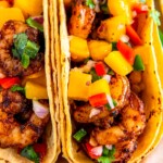 Two air fryer shrimp tacos with corn tortillas and fresh mango salsa on top.
