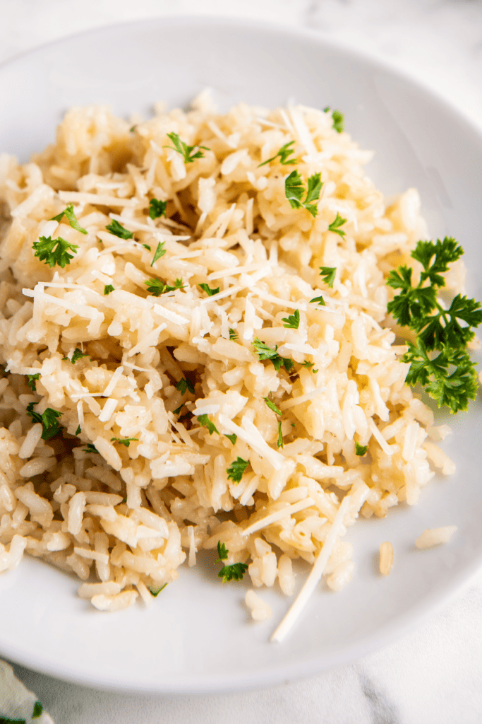 Cheesy garlic rice is served on a plate and garnished with freshly grated cheese and herbs. 