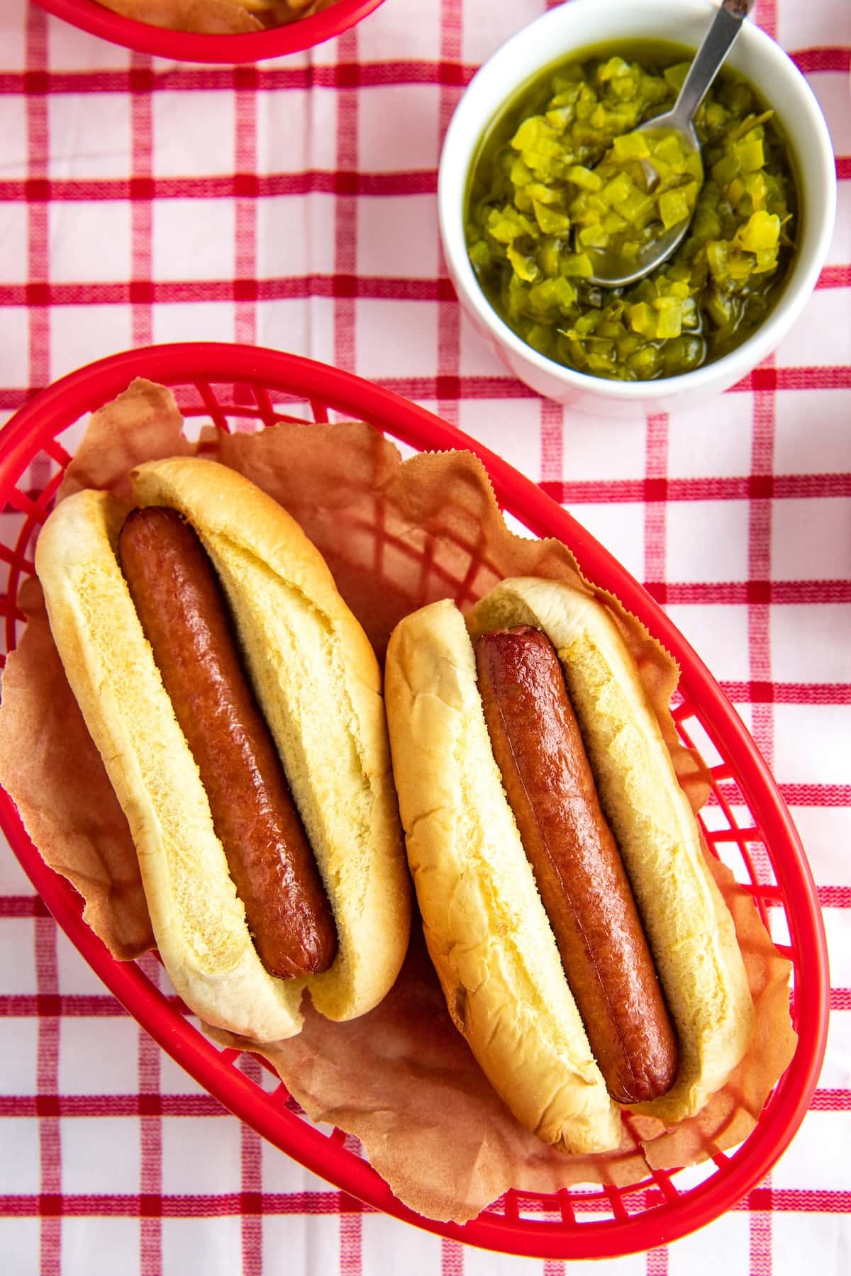 Two hot dogs in a basket next to a bowl of relish.