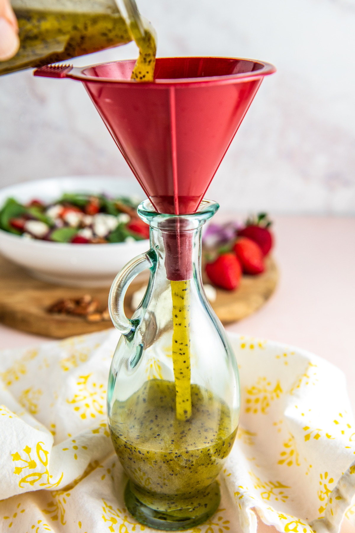 Jar of salad dressing poured through a funnel into a glass.