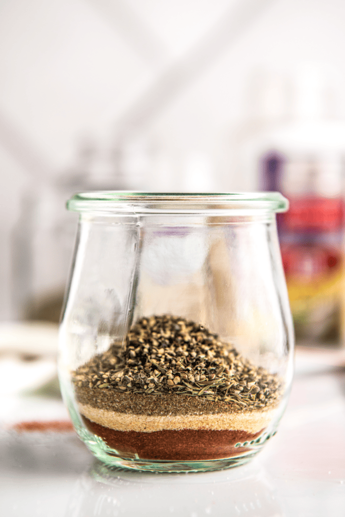 Glass jar filled with thyme, onion powder, and paprika.