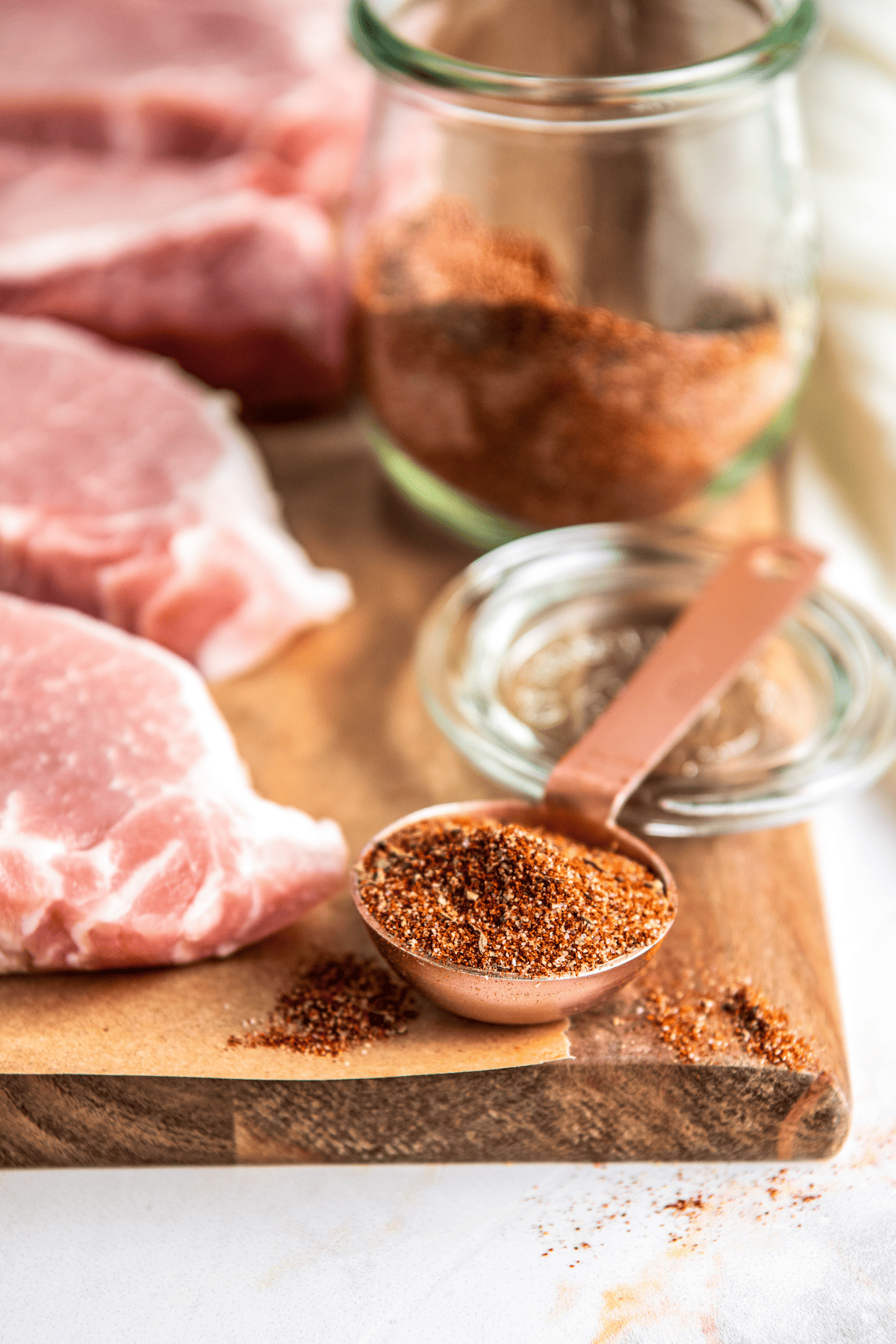 Tablespoon of pork rub next to pork chops on a cutting board.