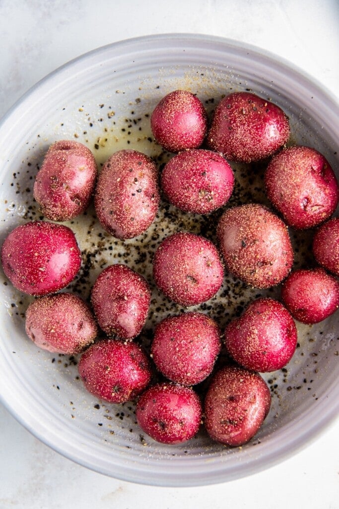 Red potatoes in a bowl with seasoning.