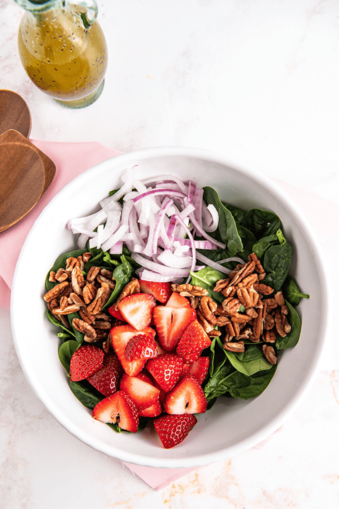 Strawberries, red onion, spinach, and pecans in a bowl.