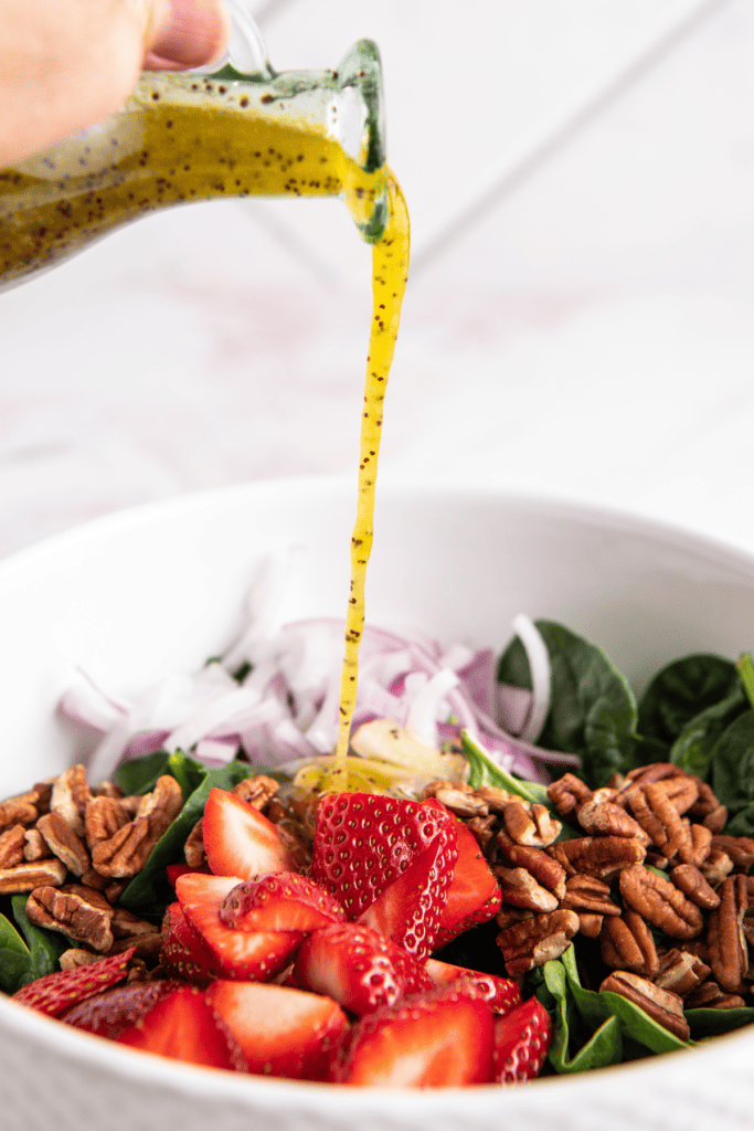 Poppy seed dressing poured over spinach and strawberry salad.