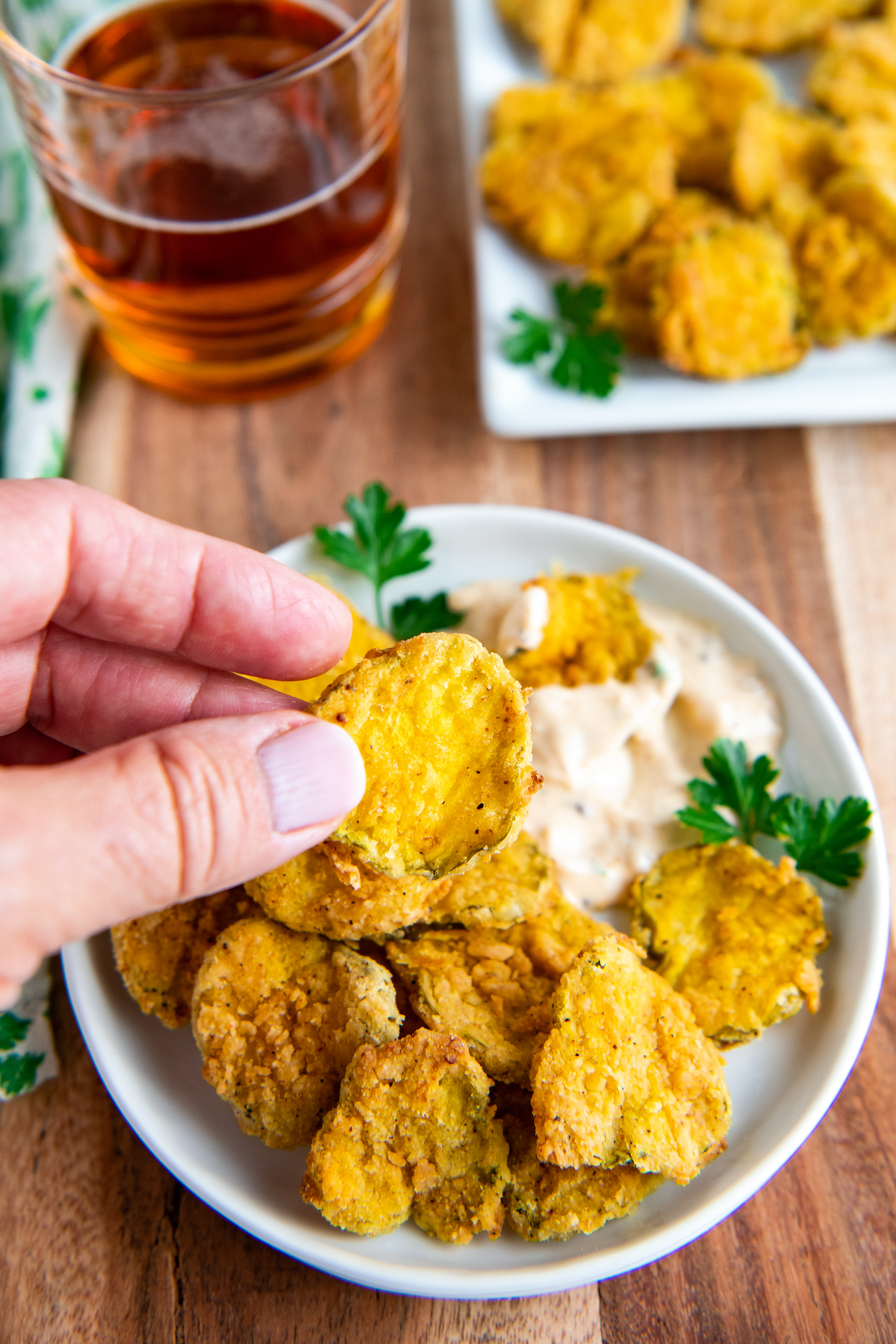 Crispy air fryer fried pickles on a plate with a dipping sauce with a hand picking up one of the fried pickles. 