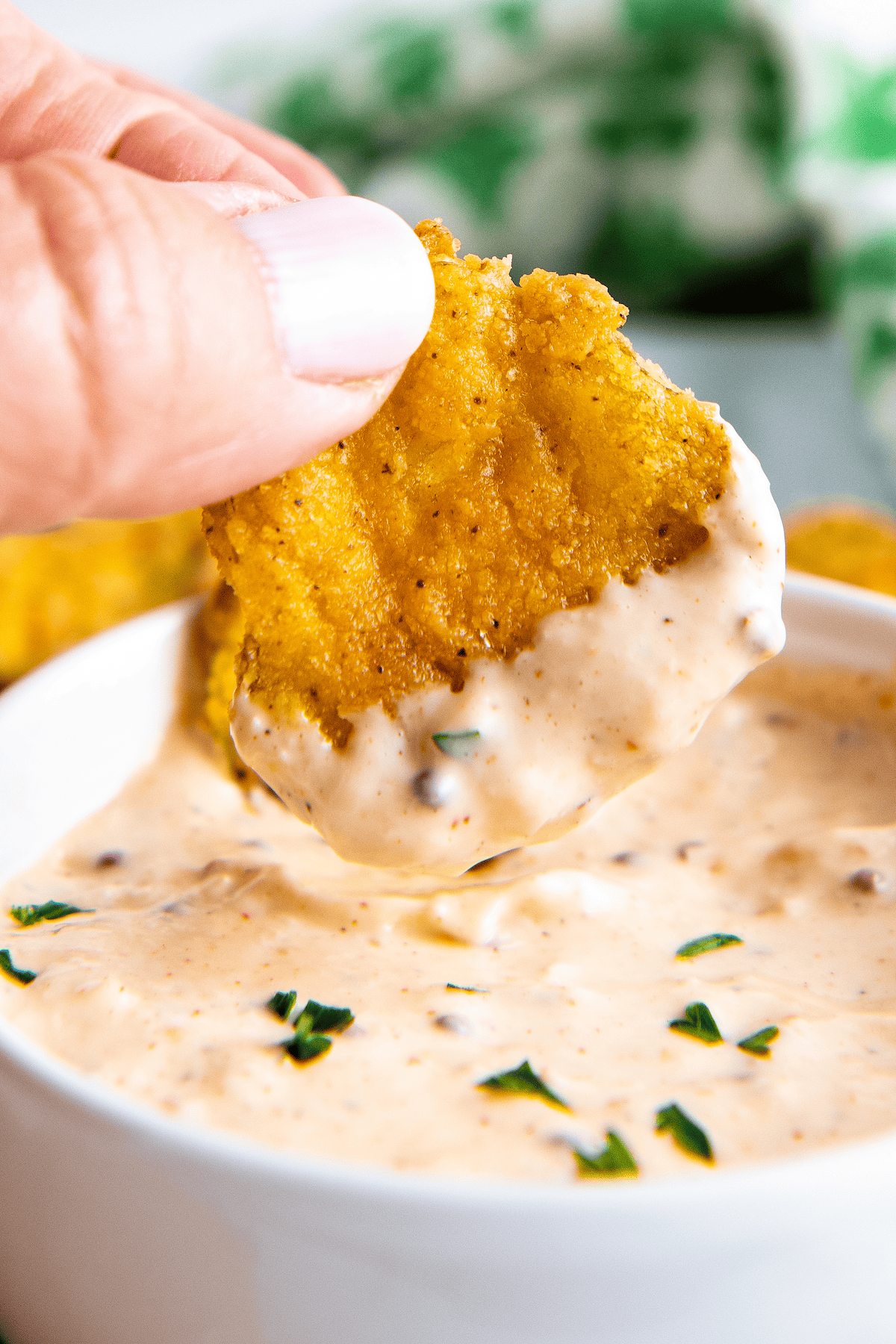 A hand dipping a fried pickle into sauce