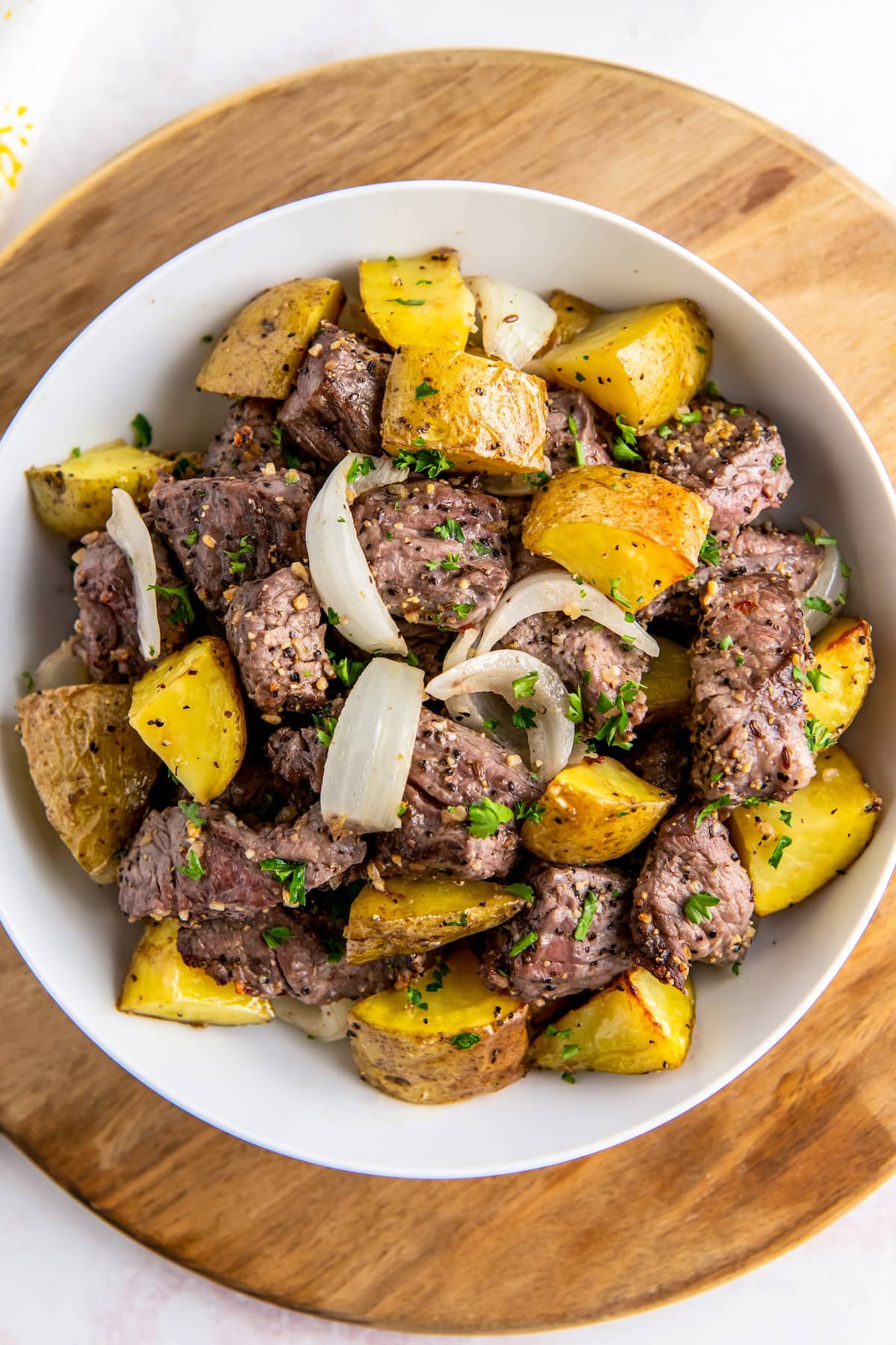 Air fryer steak bites and potatoes with onions in a bowl with fresh herbs on top.