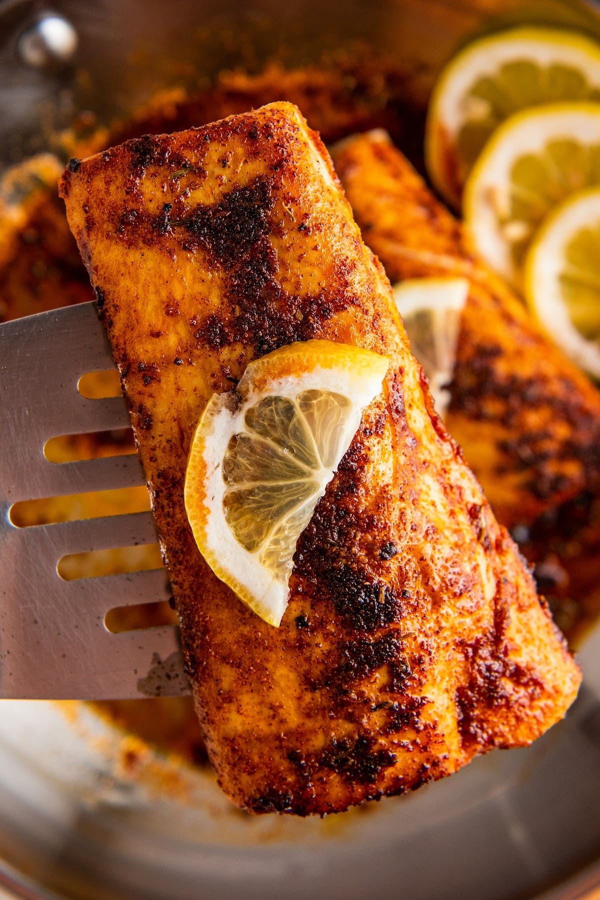 A blackened mahi mahi fillet on a spatula, topped with lemon, with more pieces in the background