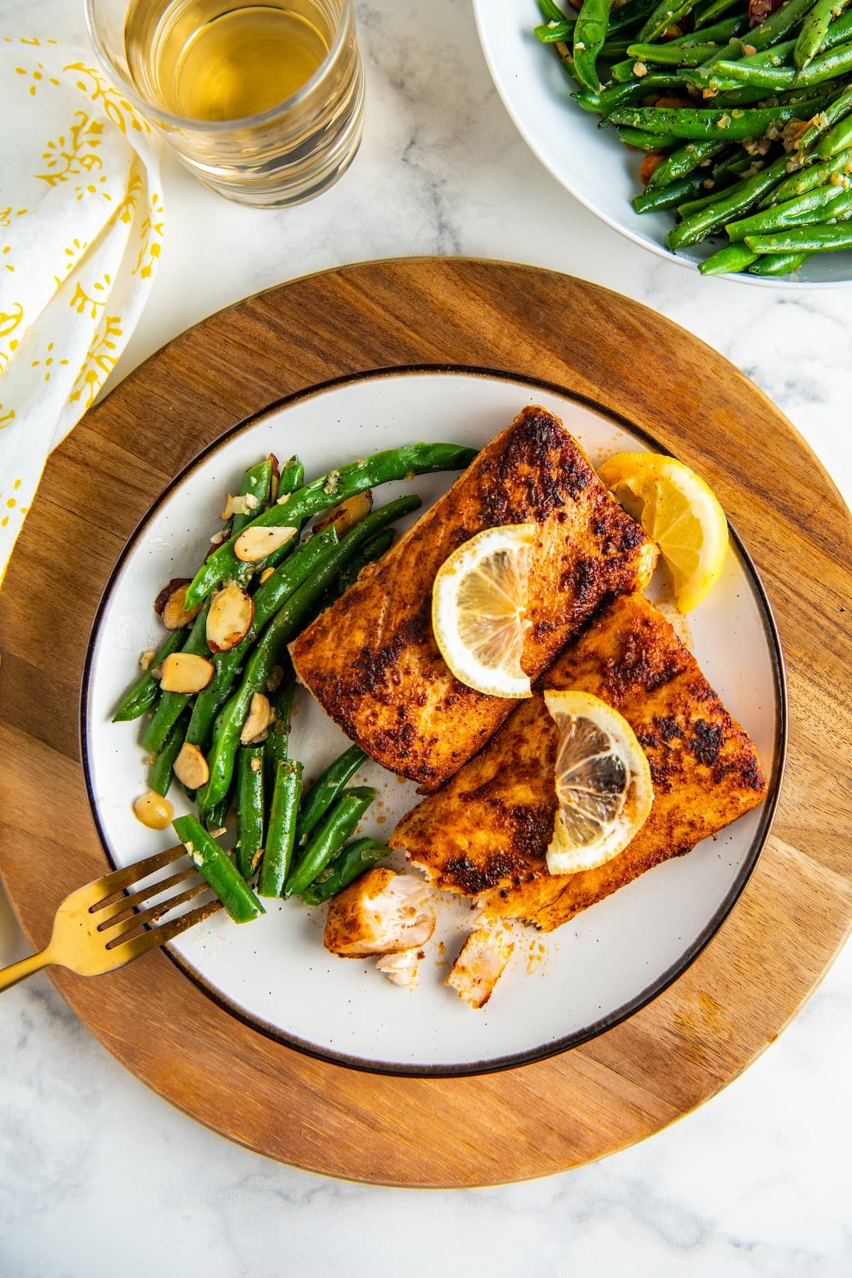 Overhead view of a plate of blackened fish topped with lemon, a side of green beans, and a fork