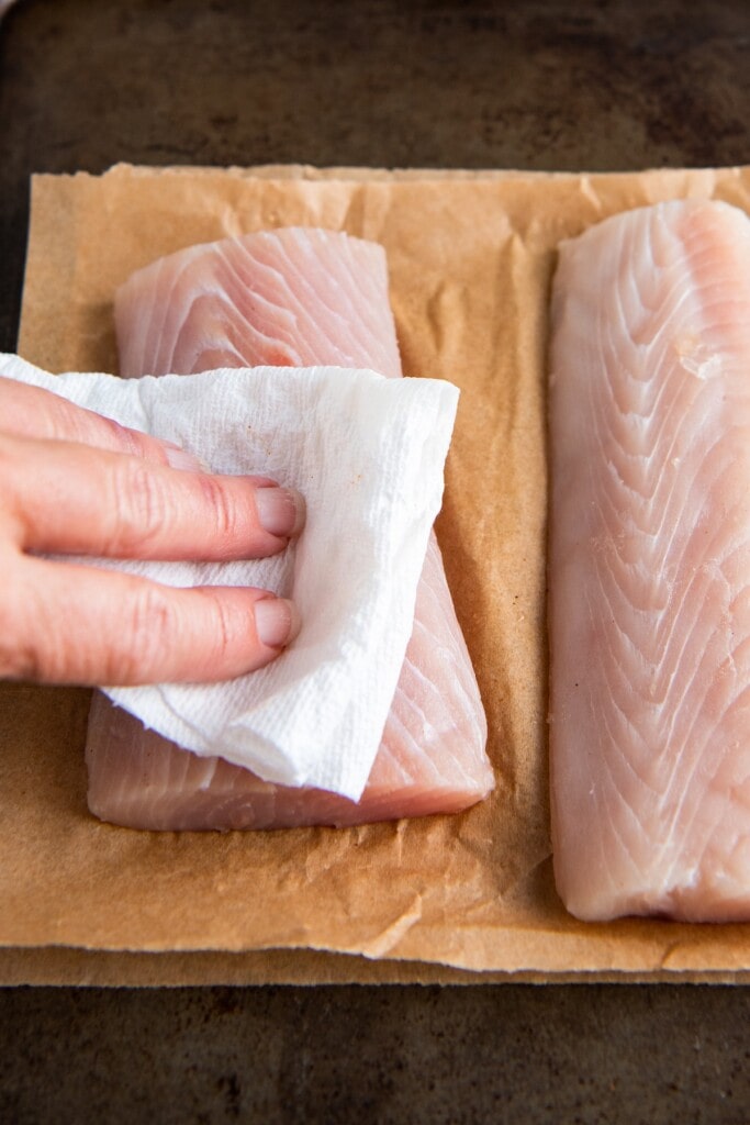 A hand drying a piece of mahi mahi with a paper towel, next to another fillet of fish