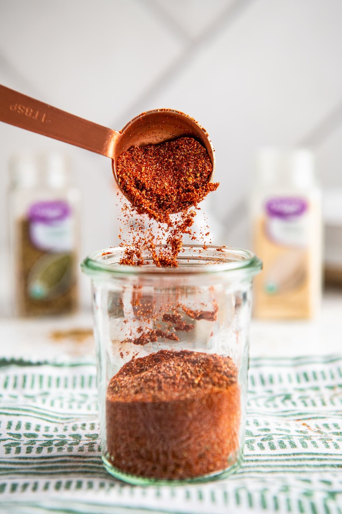 A measuring spoon pouring blackened seasoning into a jar
