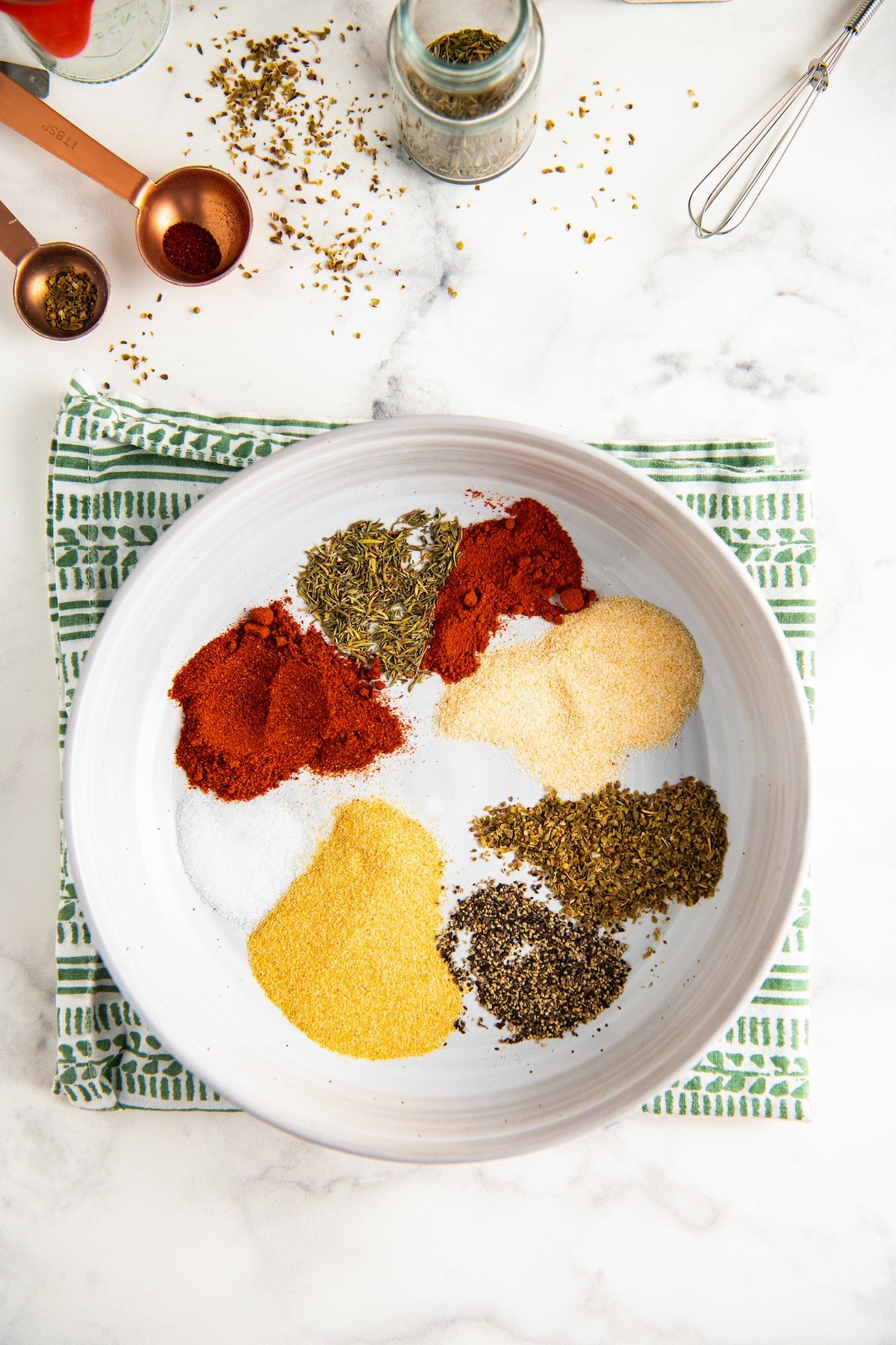 Overhead view of a bowl with piles of salt, pepper, garlic powder, onion powder, paprika, cayenne, thyme, and oregano