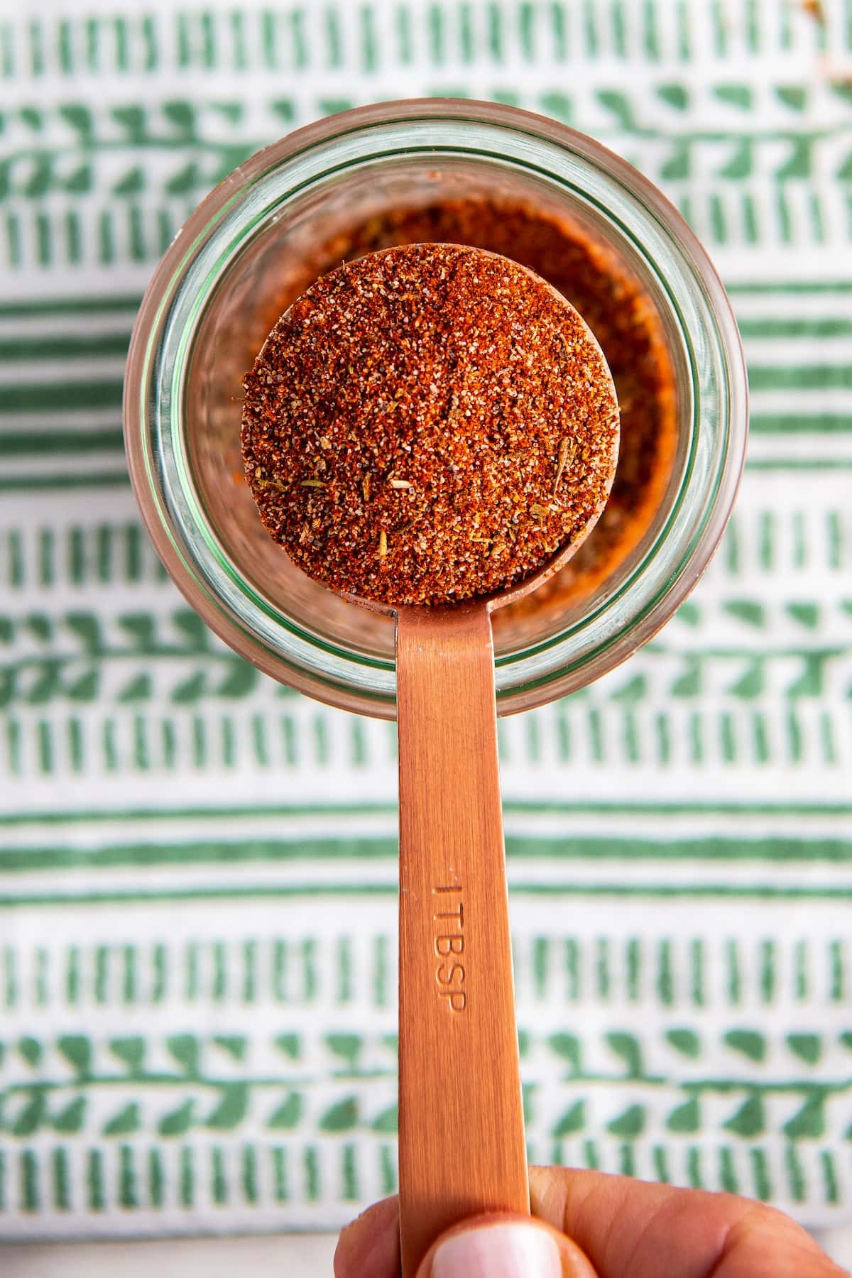 Overhead view of a measuring spoon removing a spoonful of blackened seasoning from a jar