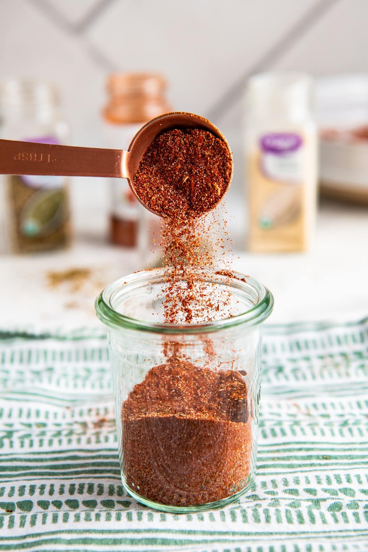 A jar of blackened seasoning with a measuring spoon pouring some of the mixture into the jar