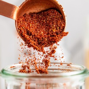 Close up of a measuring spoon pouring blackened seasoning into a jar