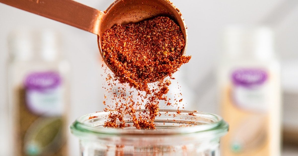 Close up of a measuring spoon pouring blackened seasoning into a jar