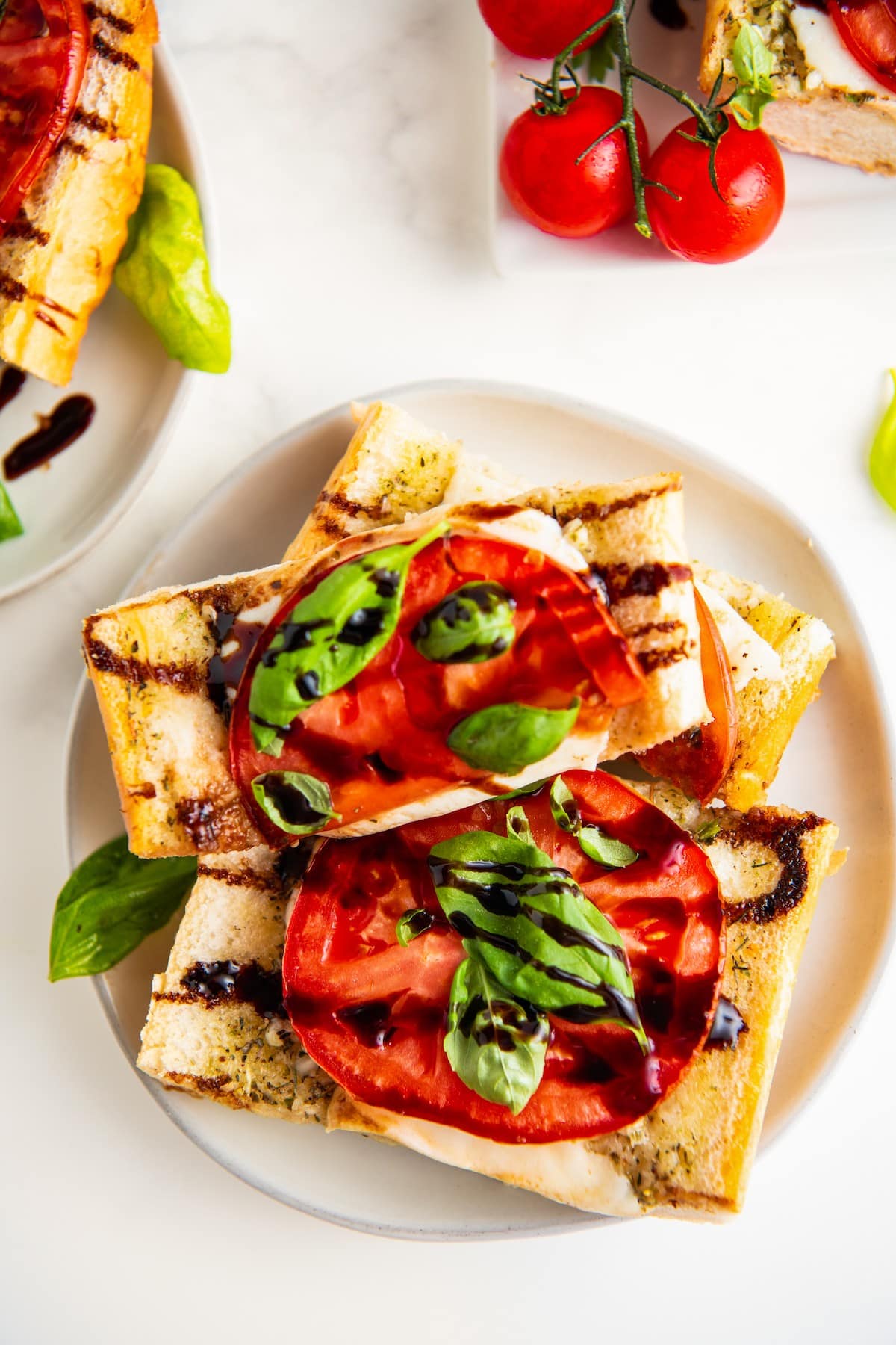 Overhead view of a plate with 3 slices of Caprese sandwiches on it, next to some fresh tomatoes