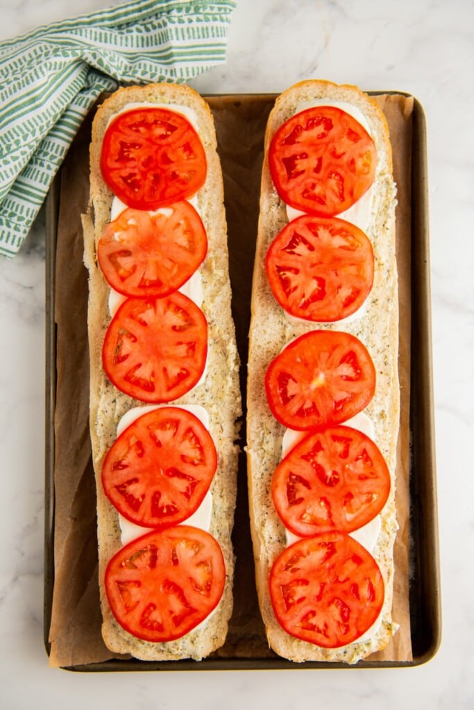 Two loaves of bread on a baking sheet topped with tomato slices