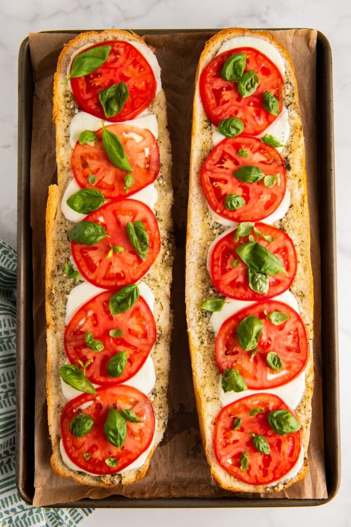 Two loaves of bread on a baking sheet topped with tomatoes and basil