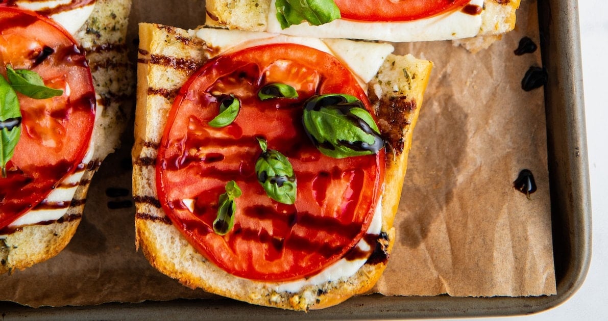 Close up of a slice of Caprese sandwich topped with basil and balsamic
