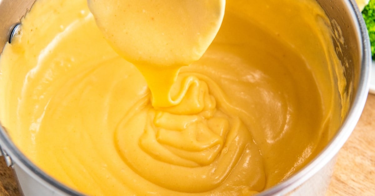 Homemade cheese sauce in a sauce pan being scooped up by a ladle.