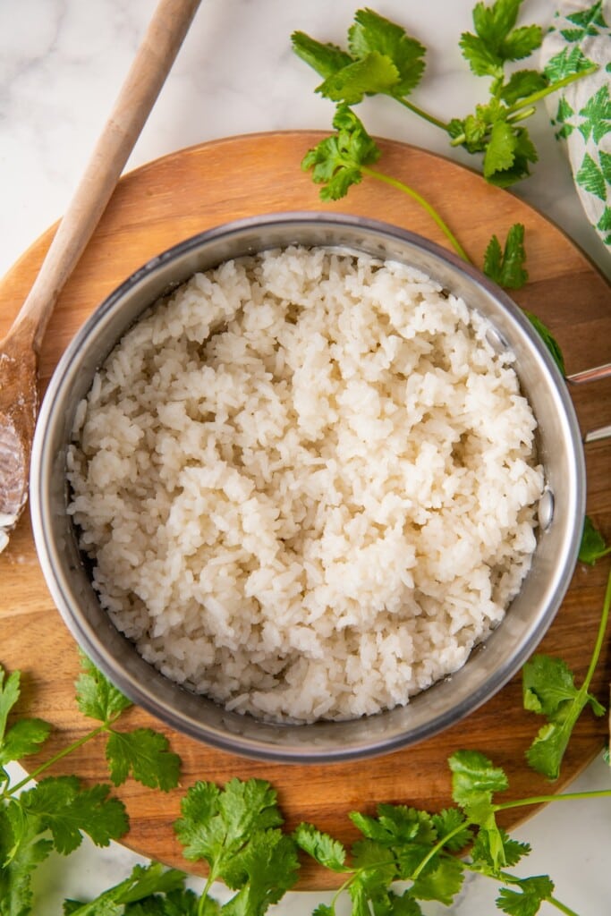 Overhead view of coconut rice in a pot, surrounded by cilantro and a wooden spoon