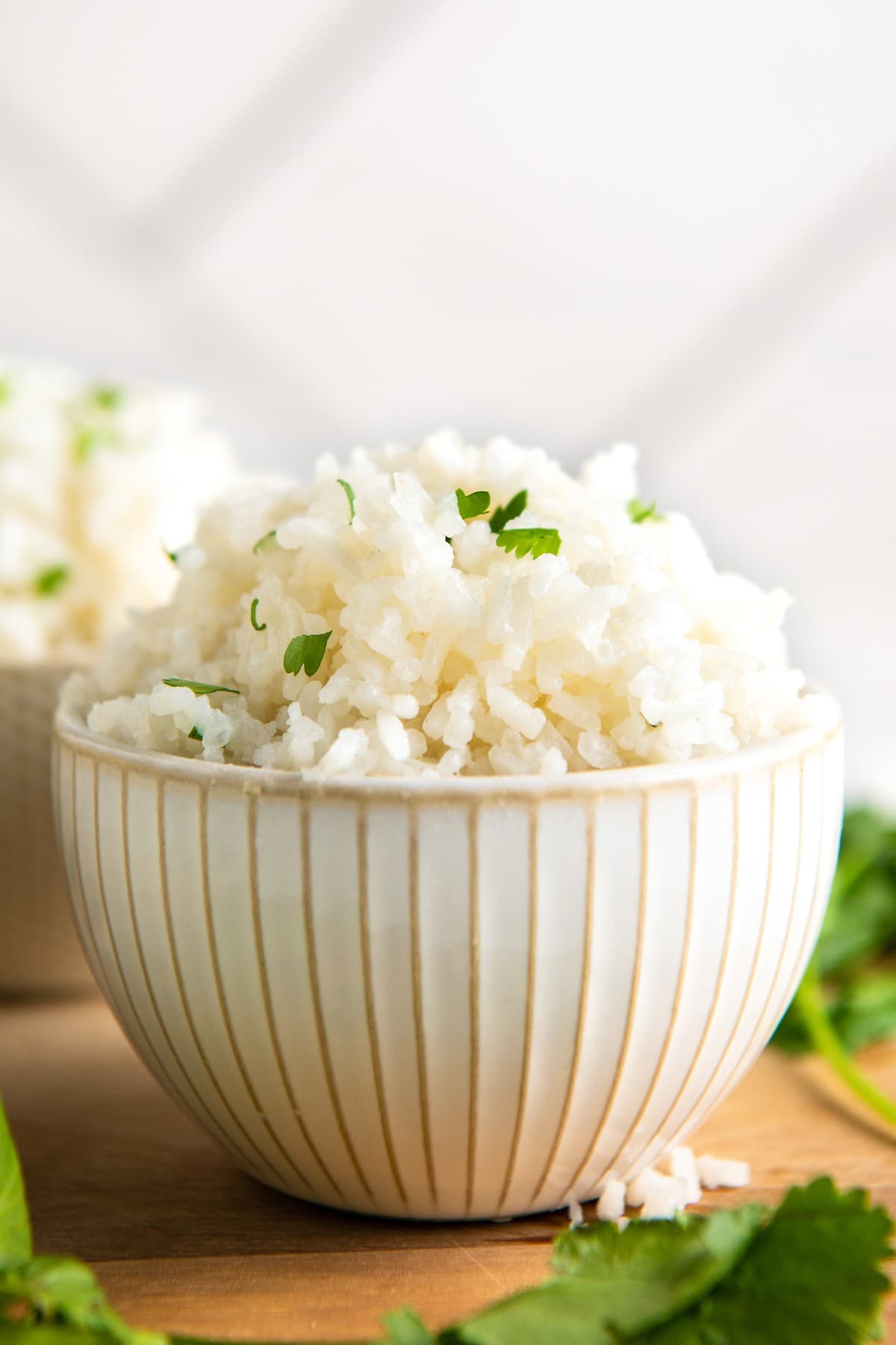 A bowl of coconut rice topped with cilantro, with another bowl in the back