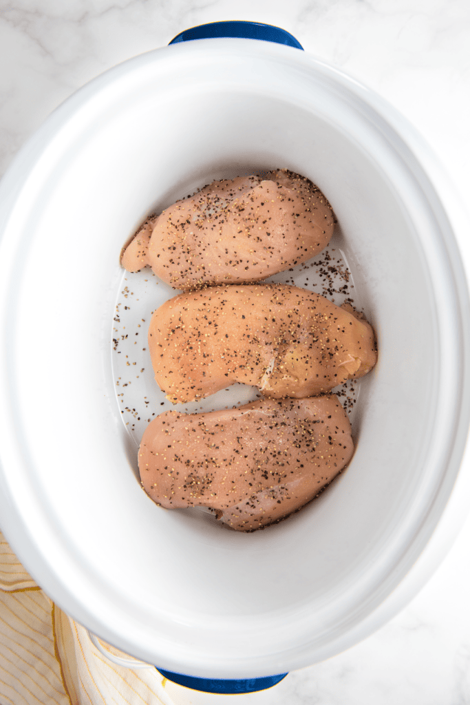 Three chicken breasts in a crock pot, seasoned with salt and pepper