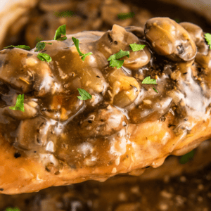 A piece of chicken marsala, covered in mushrooms, on a spoon being removed from a pot