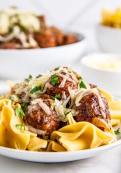 A plate of pasta and meatballs, with another plate in the background