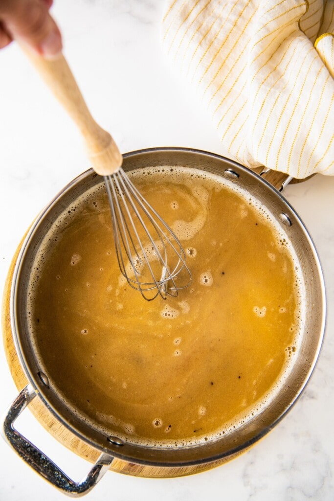 Overhead view of a pot with chicken gravy and a whisk
