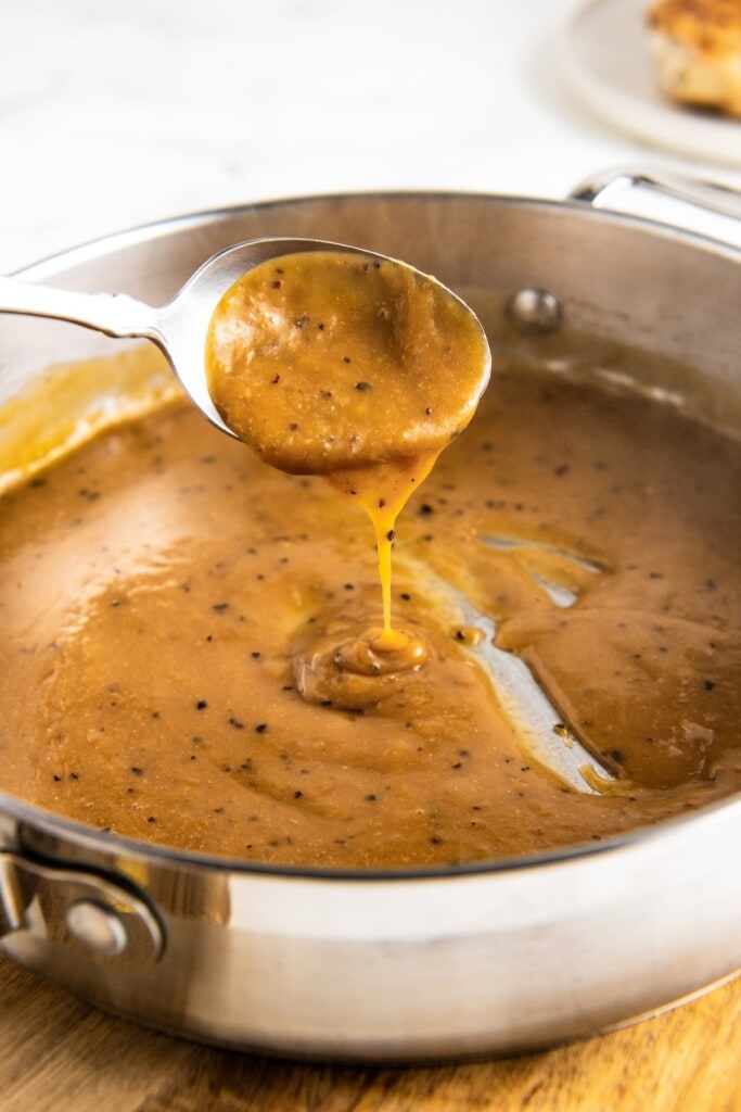 A spoon taking a spoonful of gravy out of a pan