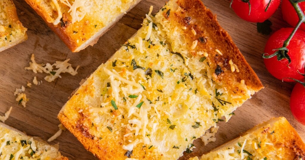 Close up of a slice of garlic bread, surrounded by more slices and cherry tomatoes