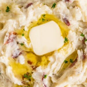 A bowl of garlic mashed potatoes with melted butter and fresh herbs on top.