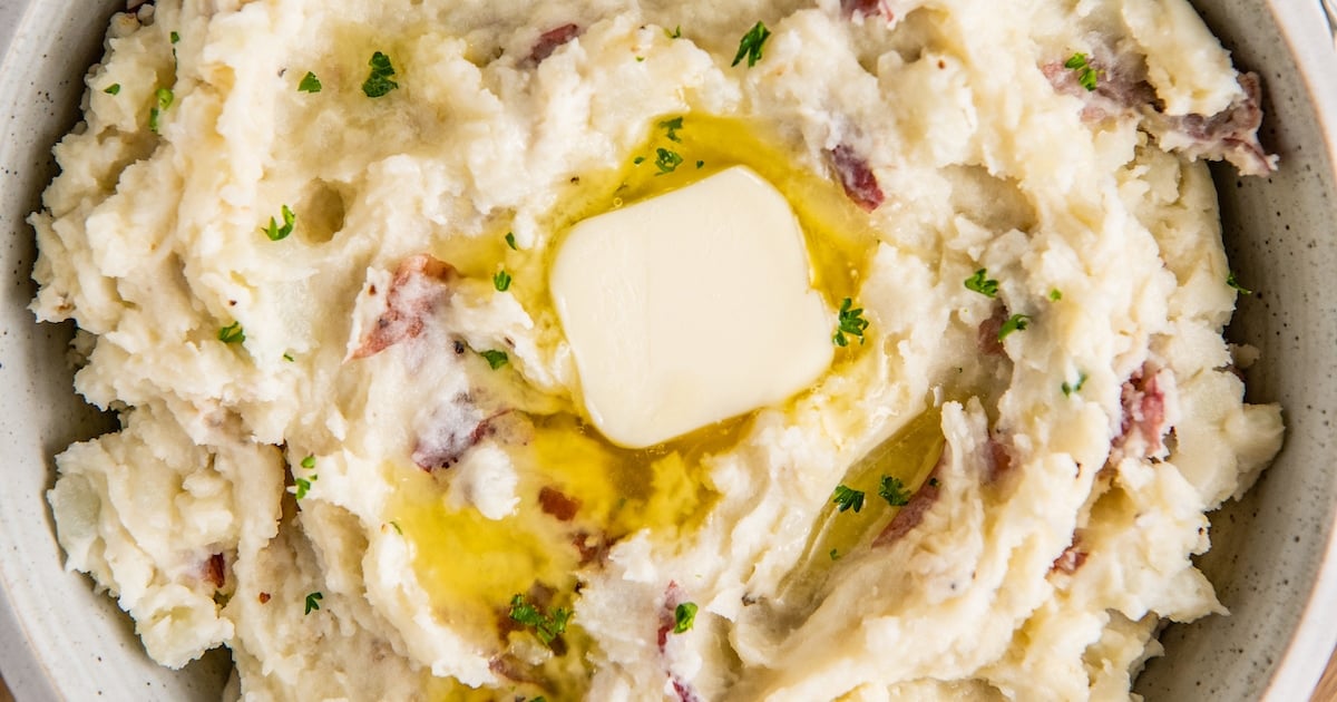 A bowl of garlic mashed potatoes with melted butter and fresh herbs on top.