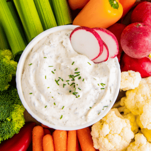A bowl of ranch with radishes in it, surrounded by carrots, radishes, broccoli, cauliflower, and celery