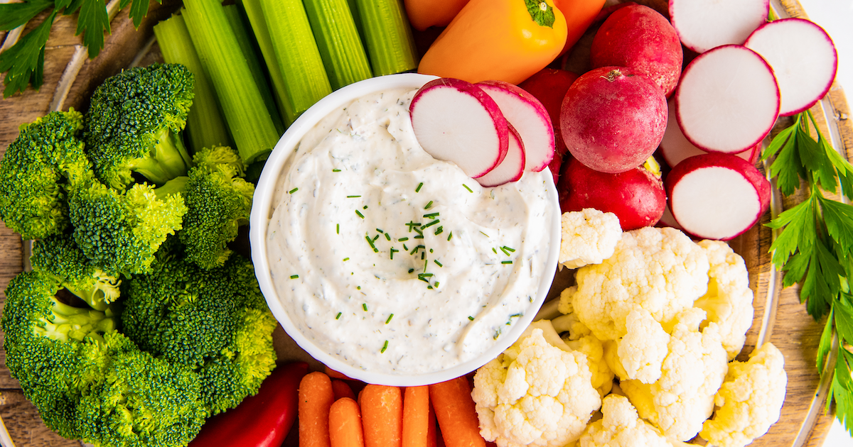 A bowl of ranch with radishes in it, surrounded by carrots, radishes, broccoli, cauliflower, and celery