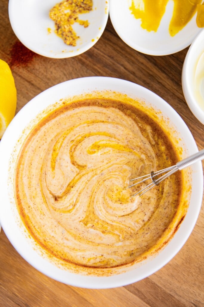 A bowl of partially-mixed honey mustard, with a whisk in it