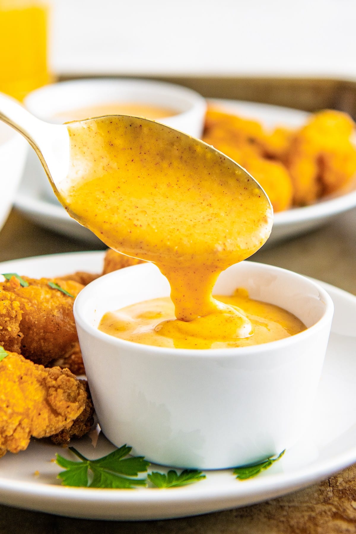 A spoon lifting out of a bowl of honey mustard, with lots of nuggets around it