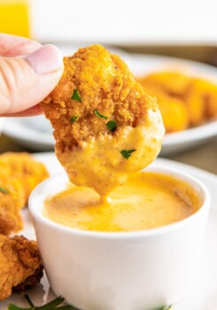 Close up of a hand dipping a chicken nugget in honey mustard