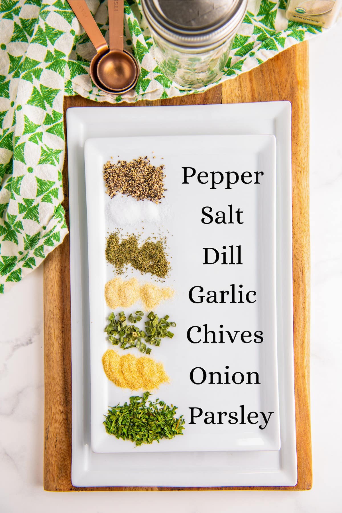 A plate with labeled piles of ingredients for ranch seasoning: pepper, salt, dill, garlic, chives, onion, and parsley.