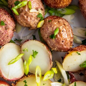 Roasted baby potatoes in a bowl, with some potatoes sliced in half, with fresh herbs sprinkled on top.