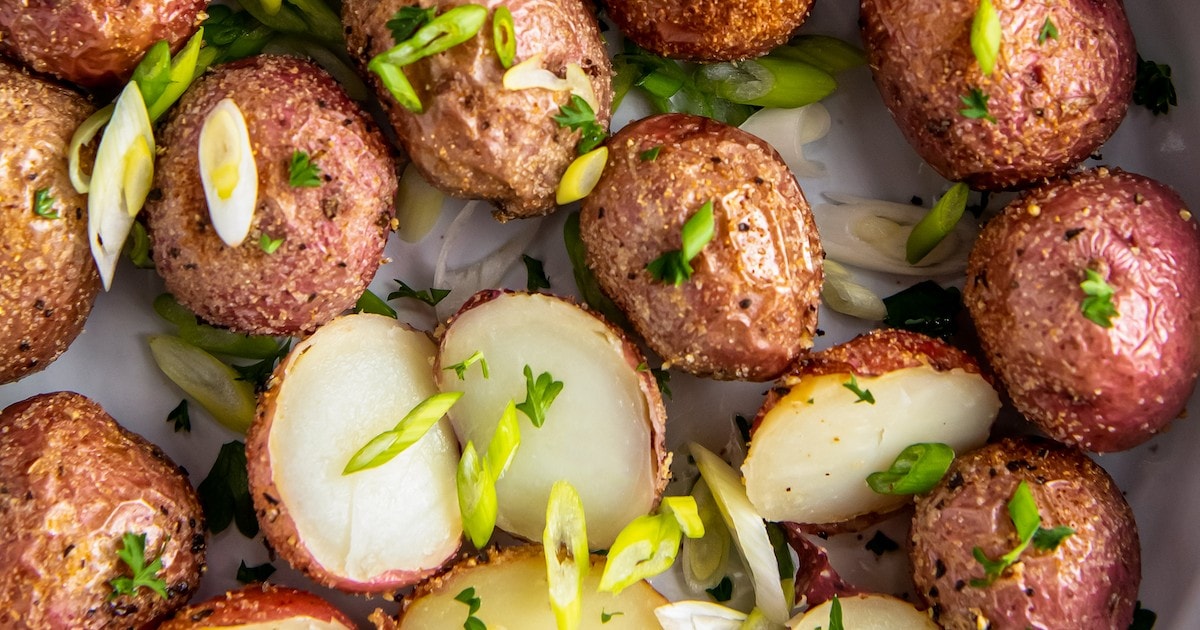 Roasted baby potatoes in a bowl, with some potatoes sliced in half, with fresh herbs sprinkled on top.