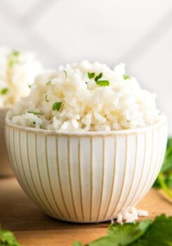 A bowl of coconut rice topped with cilantro, with another bowl in the back