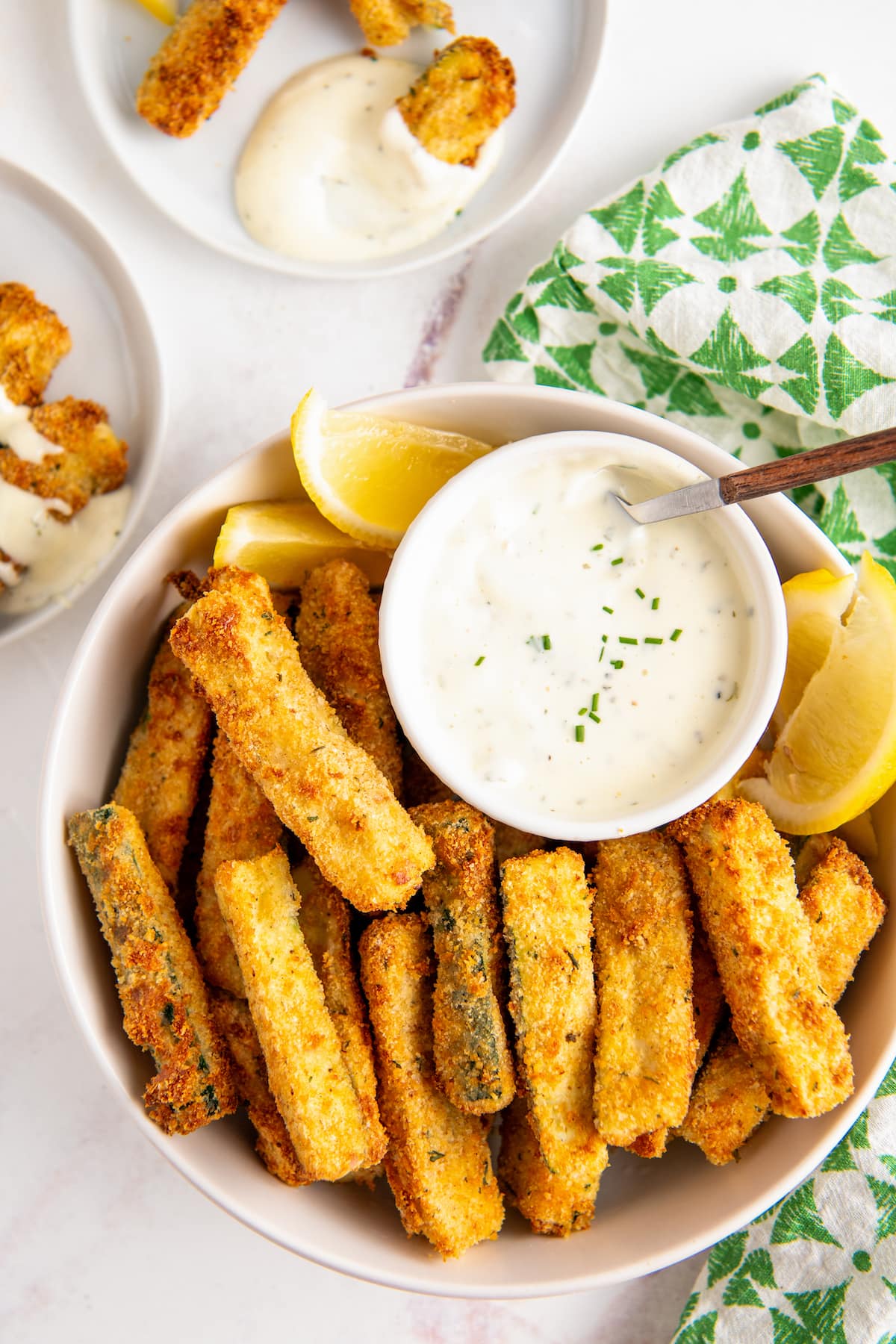 Overhead view of a plate of zucchini fries with a bowl of ranch dressing and some lemon slices