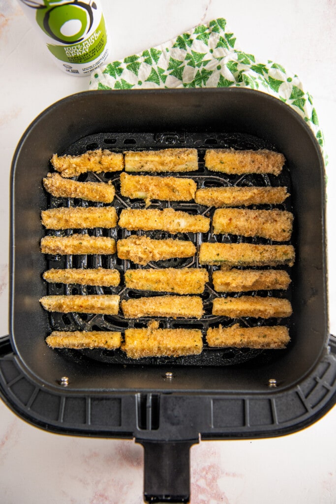 Uncooked zucchini fries in an air fryer basket