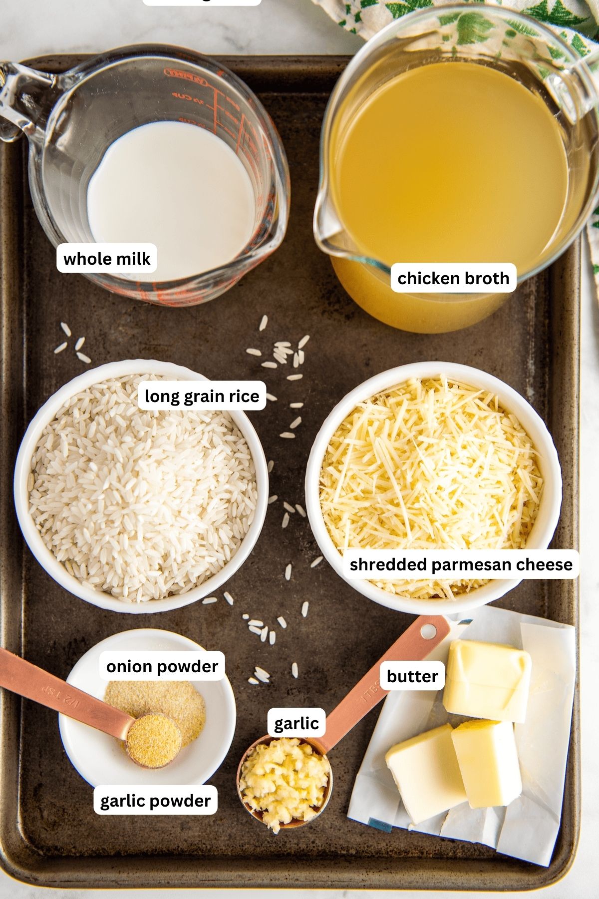 The ingredients for garlic parmesan rice recipe in order from top to bottom: whole milk, chicken broth, long grain rice, shredded parmesan cheese, onion powder, garlic powder, garlic, butter. 