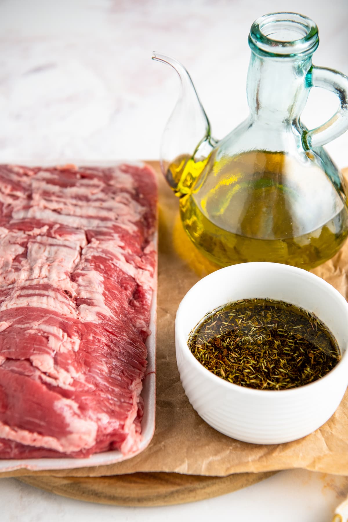 A raw skirt steak next to a jar of oil and a bowl of marinade