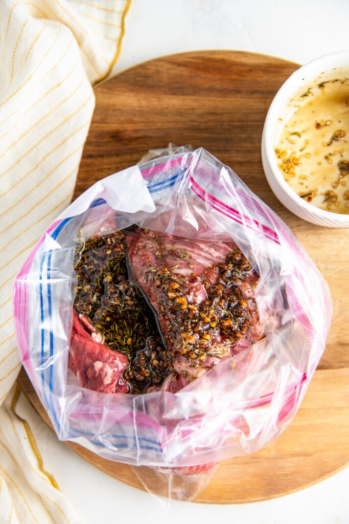 Overhead view of an open ziplock bag with raw skirt steak and marinade, next to an empty bowl